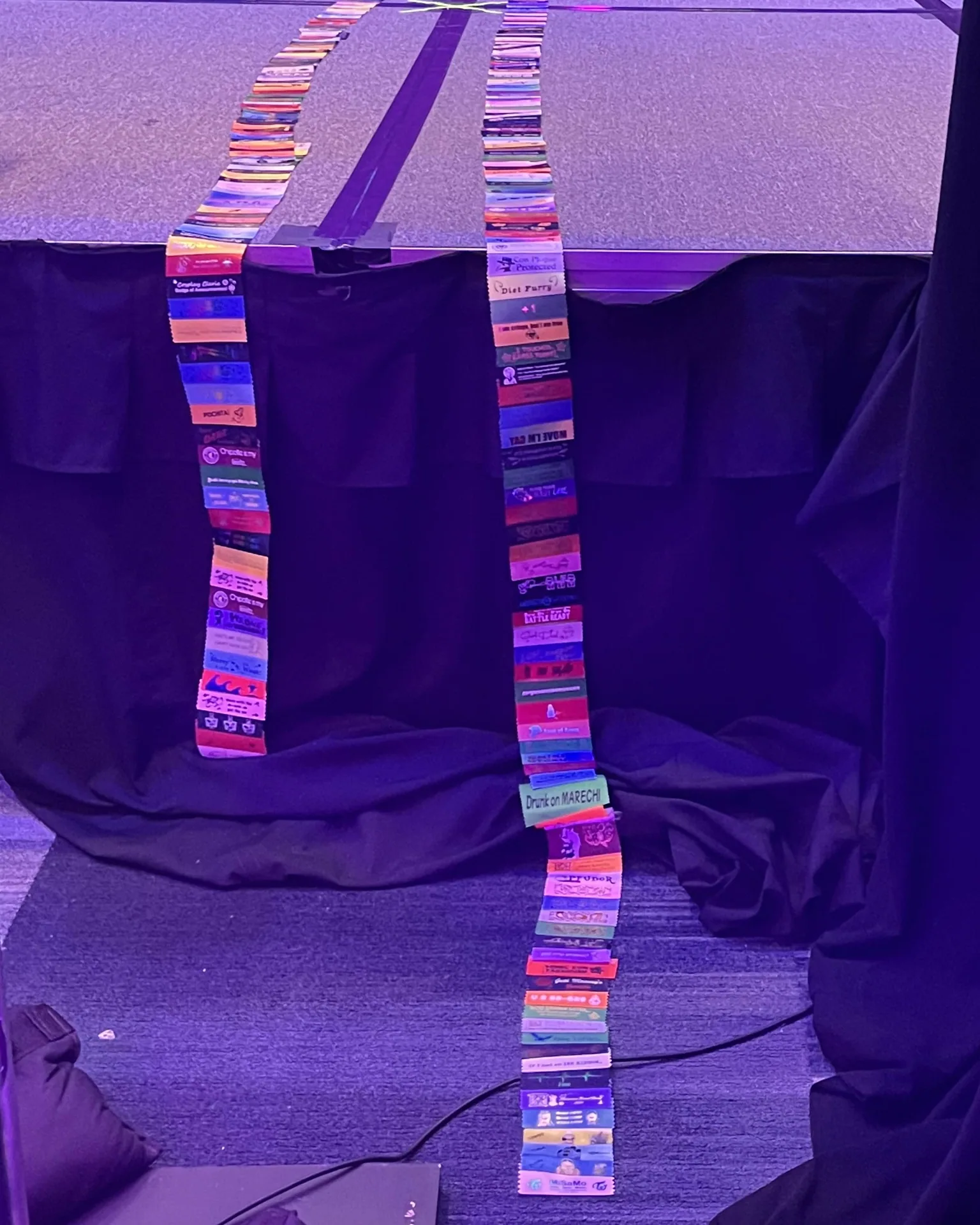 Two long chains of colorful Matsuricon badge ribbons hang over the edge of a stage.