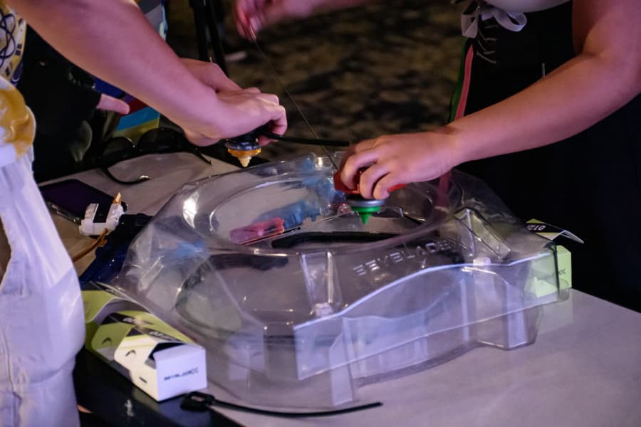 Two competitors launch Beyblades into a clear stadium during a tournament.