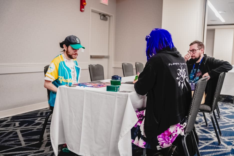 Three attendees gather around a table for a casual card game in the CCG room.