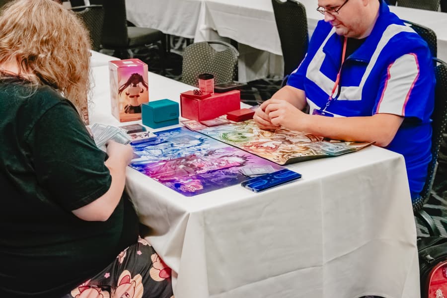 Two attendees play a trading card game across colorful playmats in the CCG room.